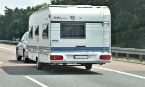Biała przyczepa kempingowa Hobby jedzie autostradą. Kierowca z kod 96 prawo jazdy wiezie rodzinę na wakacje.