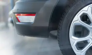 Vue rapprochée du pare-chocs arrière d'une voiture blanche, montrant un catadioptre rouge et blanc, un capteur de stationnement et une roue avec jante argentée. Le catadioptre voiture obligatoire assure la sécurité.