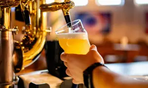 Hand holding a glass of beer being poured from a golden beer tap.