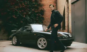Mann im Anzug und Chelsea Boots lehnt an einem Porsche.