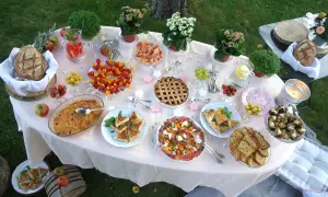 Un magnifique buffet pour une idée pique-nique : tartes, brochettes de fruits, salades, pain et boissons rafraîchissantes sur une table dressée en extérieur.
