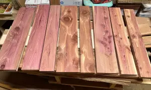 Tablones de madera de enebro con vetas rosadas y nudos visibles, apilados sobre un palé.