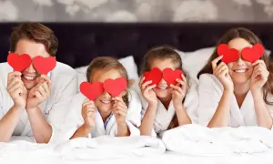 Familia feliz celebra San Valentín para niños, cubriendo sus ojos con corazones rojos en la cama.