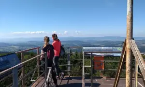 Dwie dziewczyny podziwiają panoramę z wieży widokowej na **kalenicy szczyt**. W tle rozciąga się malowniczy krajobraz Gór Sowich.