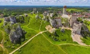 Ruiny zamków na wapiennych skałach w **parku krajobrazowym Orlich Gniazd**. Zielone wzgórza i błękitne niebo.