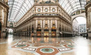 Ett tomt, lyxigt modehus i Milano med en vacker mosaikgolv och glastak. Louis Vuitton-butiken lyser upp.