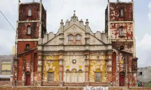 Façade d'une église à Porto-Novo, aux tours jumelles imposantes et à la peinture écaillée, avec des enfants jouant devant.