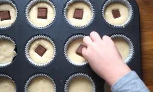 Dziecko wkłada kostkę czekolady do ciasta na muffinki. Prosty sposób, jak udekorować muffinki, by były pyszne.