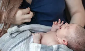 En bebis frustrerad vid amning, med öppen mun och knutna händer, insvept i en stickad filt.
