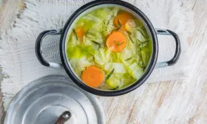 Une marmite de soupe au chou, avec des carottes et des herbes, sur une serviette blanche.