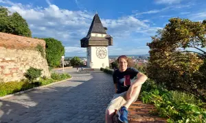 Mann sitzt vor dem Uhrturm in Graz. Ein toller Ort für graz geheimtipps mit Blick über die Stadt.