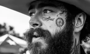 Zbliżenie na twarz Post Malone'a w czerni i bieli, z tatuażem "Tired" na policzku. Fani w Polsce czekają na jego koncert.