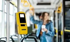 Żółty biletomat w autobusie, obok siedzeń. Kobieta w tle trzyma kubek. Pomyśl o zniżkach i ulgach na przejazdy.