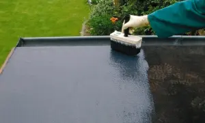 Mit einem Pinsel wird ein Bitumen-Voranstrich auf eine flache Dachfläche aufgetragen.