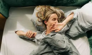 Woman in bed, covering her mouth, looking exhausted. Could this be narcolepsy vs hypersomnia?