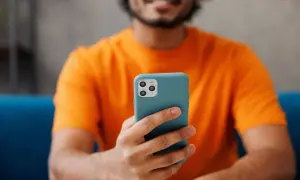 Uśmiechnięty mężczyzna w pomarańczowej koszulce trzyma telefon. Chcesz wiedzieć, jak sprawdzić czas korzystania z telefonu?