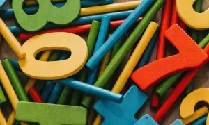Bunte Holzfiguren und Stäbchen, die ein Helfersystem Grundschule bilden. Zahlen wie 0, 7 und 8 sind erkennbar.