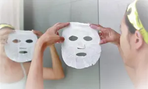 Una donna si prepara per una maschera viso, riflettendosi allo specchio. Scopri quando farla per una pelle radiosa.