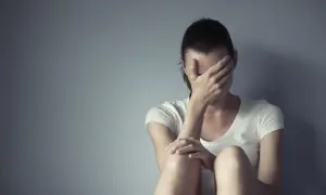 Kobieta siedzi przy ścianie, zakrywając twarz dłońmi. Czuć jej deprexolet.