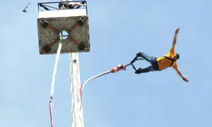 Odwaga w czystej postaci: mężczyzna w żółtej koszulce wykonuje ekscytujący skok na bungee, szybując w błękitnym niebie.