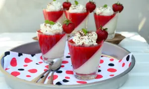 Panna cotta z truskawkami i bitą śmietaną w szklankach, udekorowana miętą i czekoladą.