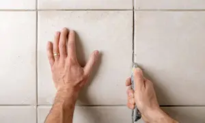 Main tenant utilise un cutter pour enlever des joints de carrelage en ciment.