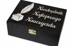 Czarna szkatułka z piórem i kałamarzem, ozdobiona napisem "Niezbędnik Najlepszego Nauczyciela". Idealna dedykacja dla nauczyciela.