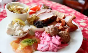 En härlig tallrik med godsaker på julbordet: lax, köttbullar, sill, ägg, rödbetor, korv och en liten skål med gratäng.
