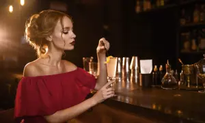 Elegancka kobieta w bordowej sukience z koktajlem w dłoni, idealne paznokcie do bordowej sukienki.