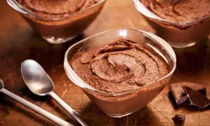 Trois coupelles de mousse au chocolat sans oeuf, onctueuse et gourmande, avec des morceaux de chocolat noir et des cuillères sur fond de bois.