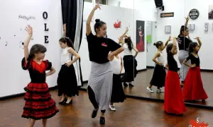 Niñas aprenden baile flamenco en una clase. La maestra las guía con movimientos elegantes.