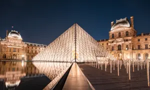 Das Louvre-Museum in Paris bei Nacht, mit der beleuchteten Glaspyramide im Vordergrund und dem historischen Gebäude im Hintergrund.