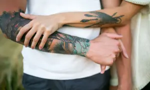 Dłonie obejmują się na tle tatuaży. Alantan Plus na tatuaż dba o skórę, by kolory były żywe.