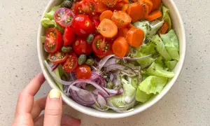 Deliciosa ensalada mediterránea con lechuga, tomates cherry, zanahoria, cebolla morada y alcaparras.