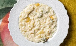 Un cremoso risotto pere e gorgonzola, servito su un piatto bianco decorato, con pezzetti di pera e formaggio blu visibili.