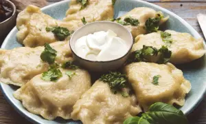 Pyszne pierogi ze szpinakiem i serem feta, udekorowane natką pietruszki, podane z kleksem śmietany.