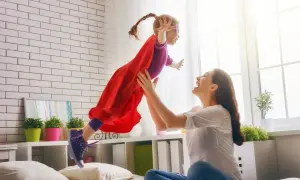 Mama rzuca córkę w stroju superbohaterki w powietrze. Radość i zabawa w pokoju.