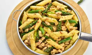 Penne z kurczakiem i szparagami, posypane płatkami chili, w metalowej misce na drewnianej desce.