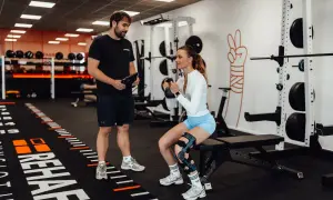 Mann mit Tablet beobachtet Frau beim Kniebeugen-Training mit Kettlebell. Meniskus Training statt OP ist hier das Ziel.