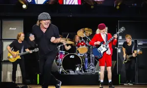 Zespół AC/DC na scenie, grający swoje kultowe utwory. Wokalista w czapce, gitarzysta w czerwonym stroju.