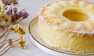 Delizioso chiffon cake ricetta originale americana, leggero e soffice, spolverato di zucchero a velo, con fiori secchi sullo sfondo.