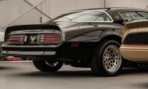 Błyszczący czarny muscle car z charakterystycznym spojlerem i felgami. Obok złoty klasyk.