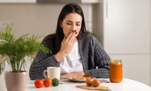 Donna con nausea e debolezza alle gambe si copre la bocca, seduta a tavola con colazione.