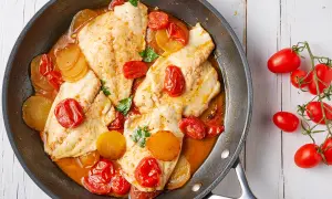 Orata in padella con pomodorini e patate, un piatto succulento e colorato, pronto per essere gustato.