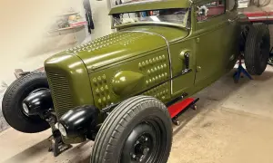 Grön hot rod, en klassisk bilbyggare USA, står på pallbockar i ett garage.