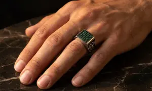 Anillo de plata con piedras verdes, puesto en el dedo anular, el dedo en que se pone un anillo normal.