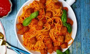 Un piatto invitante di spaghetti con polpette, conditi con salsa rossa e guarniti con foglie di basilico fresco.
