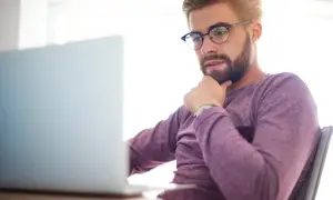 Mężczyzna w okularach zamyślony nad ekranem laptopa. Zastanawia się, krd co to znaczy dla jego pracy.