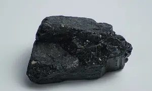 Ein glänzender, schwarzer Stein, der an einen Brocken Onyx erinnert, liegt auf weißem Grund.