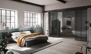 Ein gemütliches **Bett unter Fenster** mit industriellem Charme. Daneben ein offener Bereich mit Badewanne und Waschbecken.